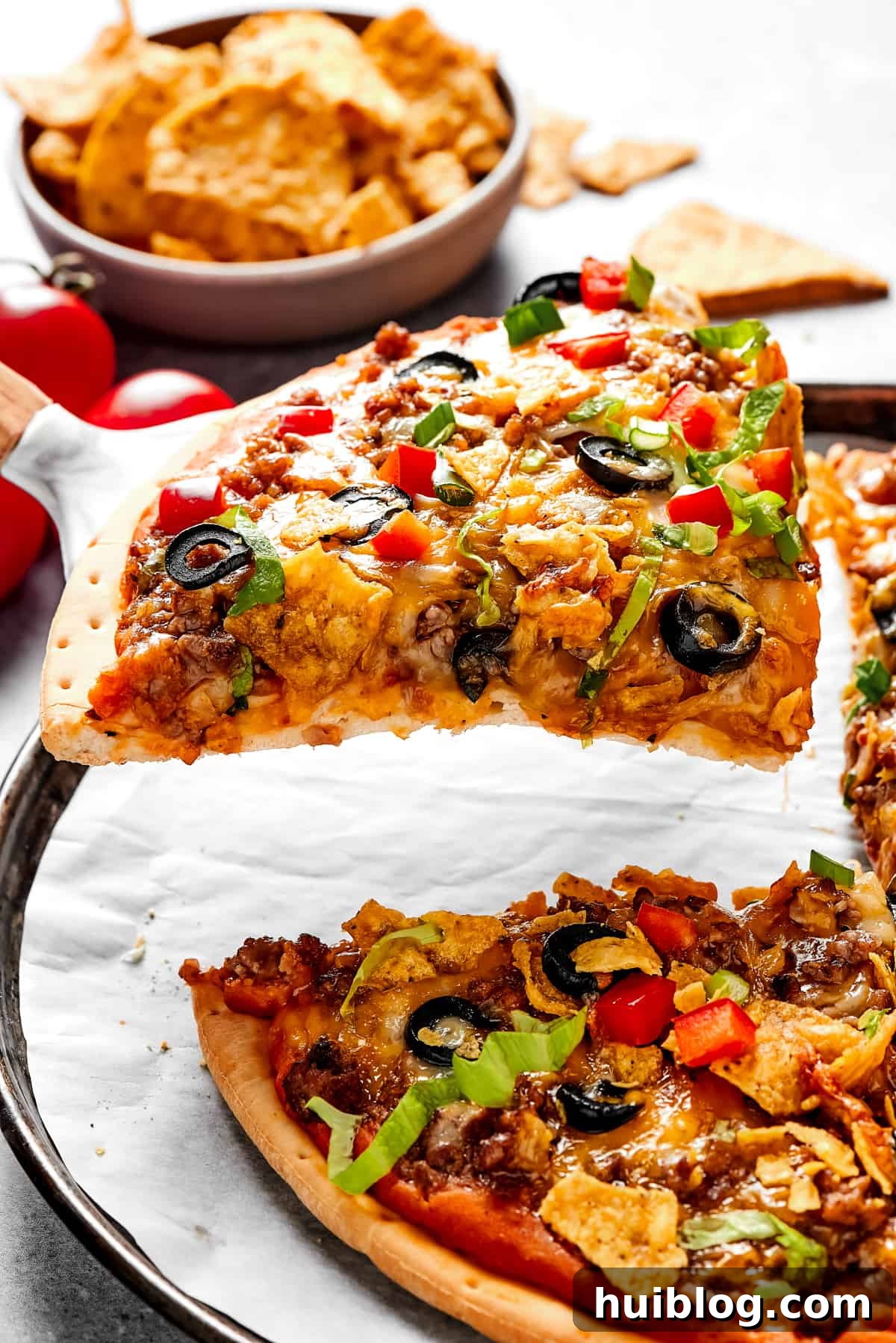 Ready to Enjoy: A Slice of Taco Pizza A beautifully sliced taco pizza, with one perfect slice carefully lifted with a pie server, ready to be served. Another slice rests on a small, rustic plate in the background.