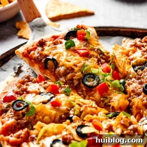 Lifting a slice of taco pizza with a pie server, showcasing the rich layers and textures.