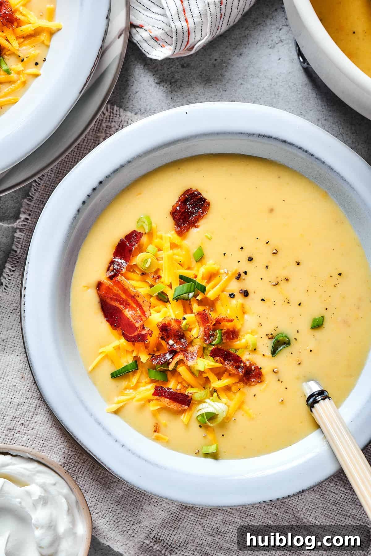 A steaming bowl of loaded baked potato soup, generously topped with crispy bacon bits, shredded cheddar cheese, and freshly chopped green onions.