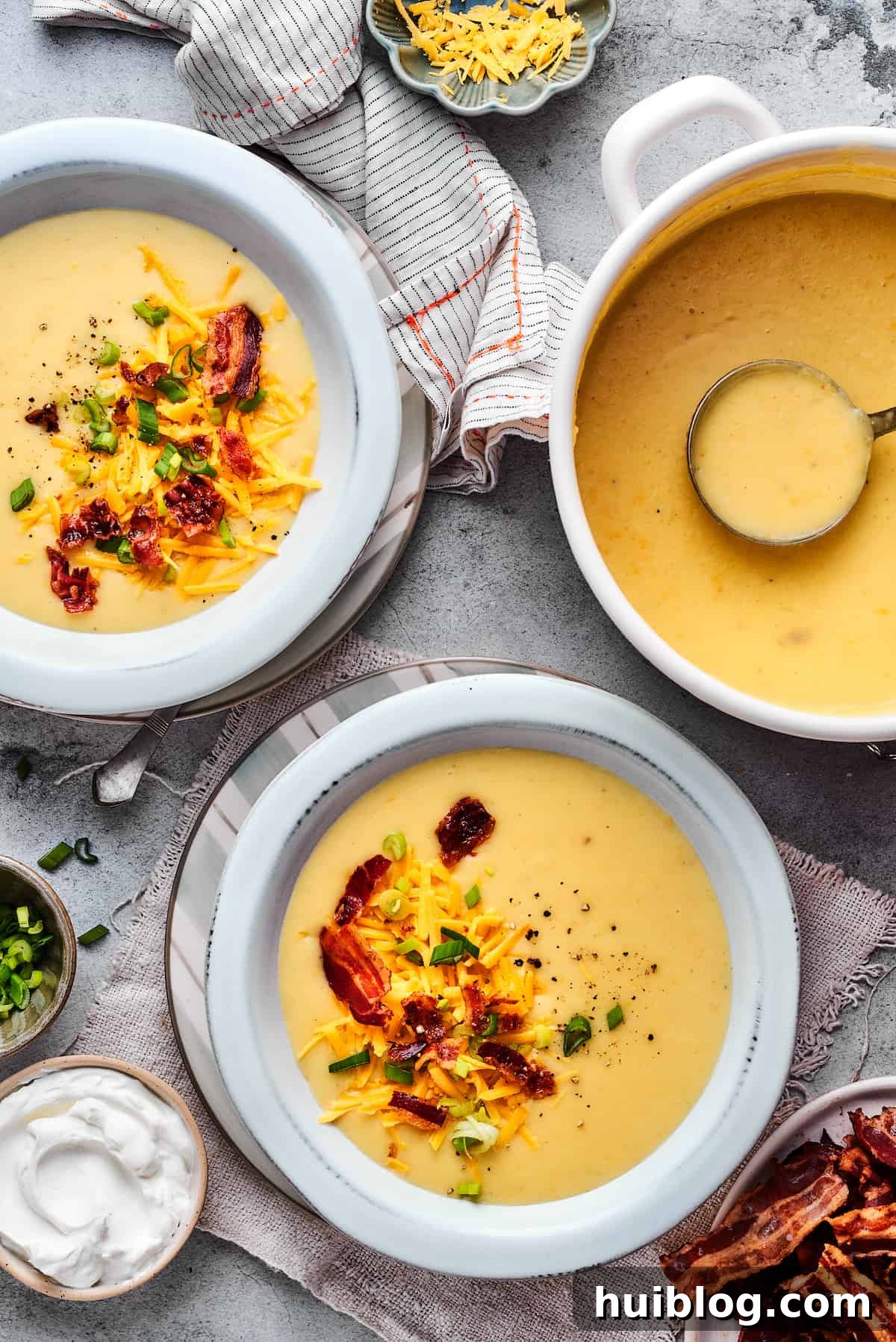 A large pot of hot, creamy baked potato soup sits beside two individual bowls, each beautifully garnished and ready to be enjoyed.