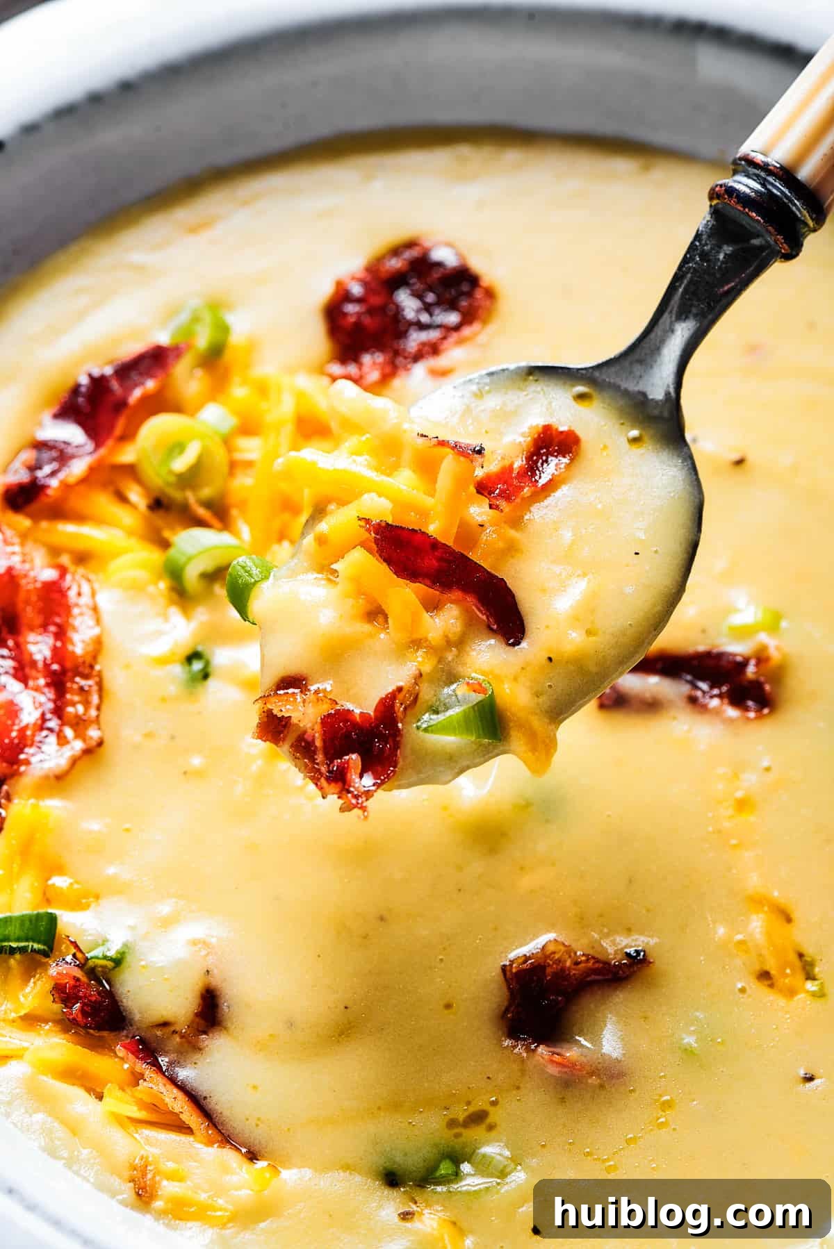 A pristine white bowl filled with creamy, loaded baked potato soup, with a spoon gently lifted out, displaying the soup's rich texture and inviting warmth.