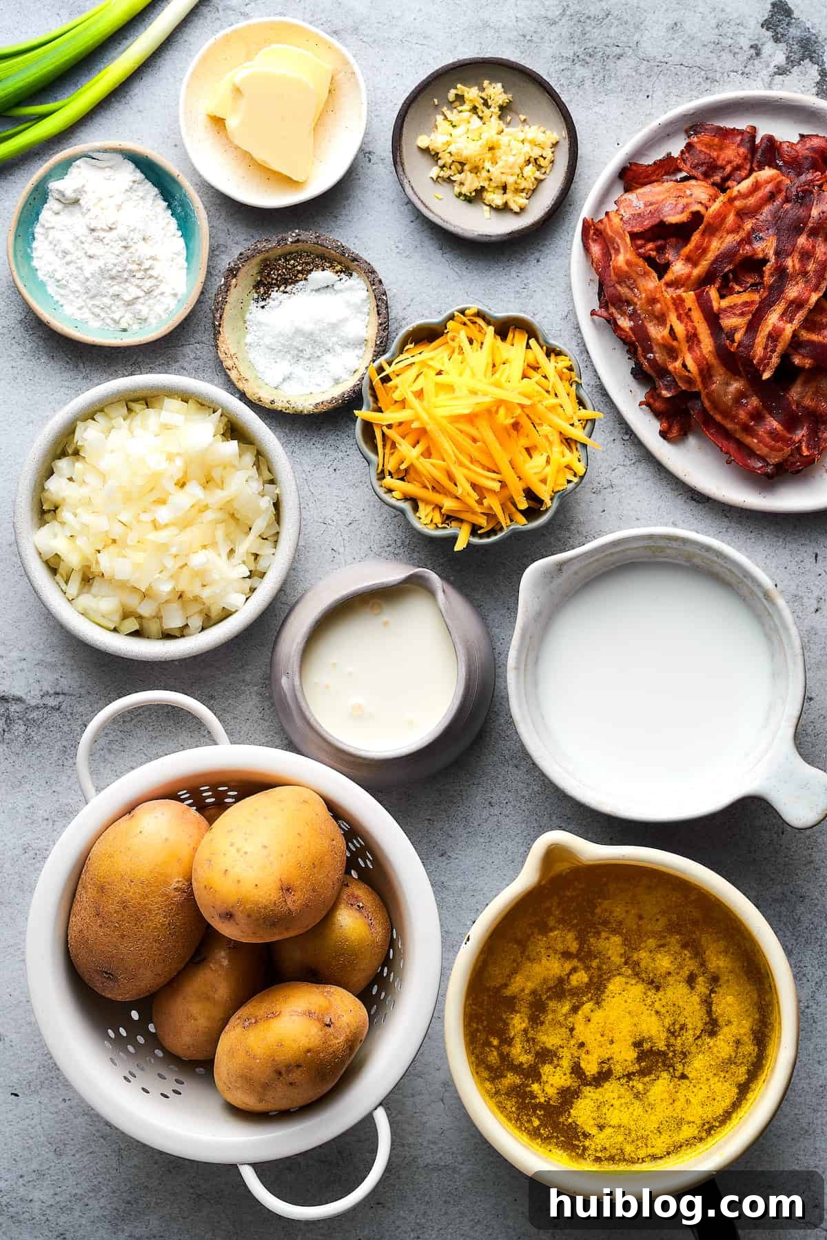 All the fresh ingredients for a delicious baked potato soup, including potatoes, cheese, bacon, and herbs, neatly arranged on a rustic wooden surface.