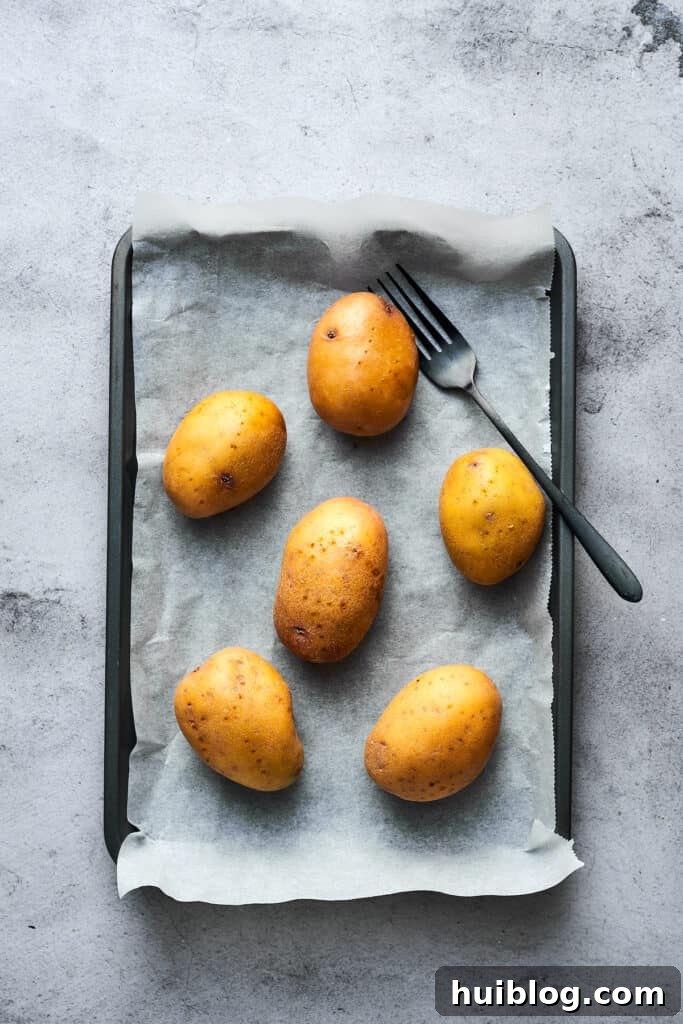 Potatoes freshly washed, pricked with a fork, and carefully arranged on a baking sheet, ready for the oven.
