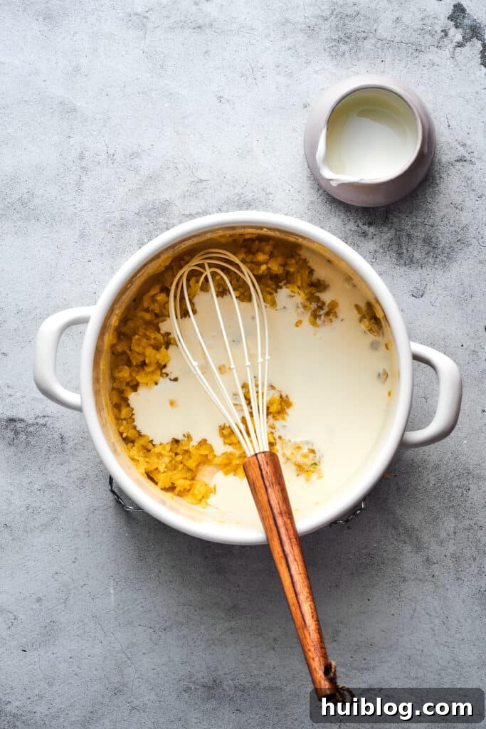 A steady stream of milk being whisked into the roux in a soup pot, gradually creating a creamy base.