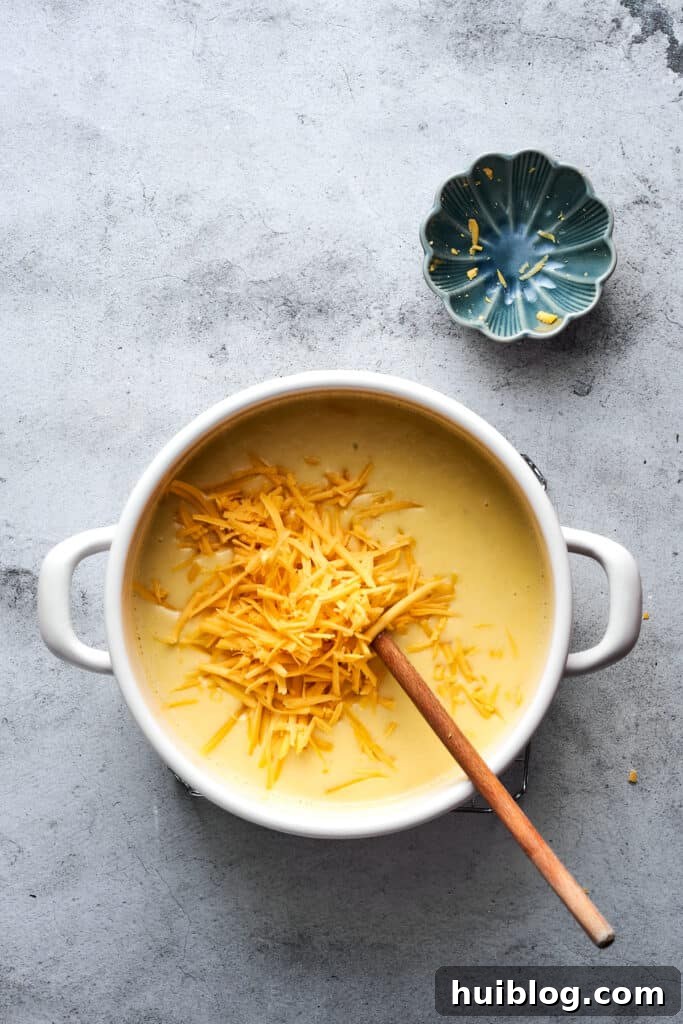 A generous amount of shredded cheddar cheese being stirred into a pot of hot, creamy soup, melting to enrich the flavor and texture.