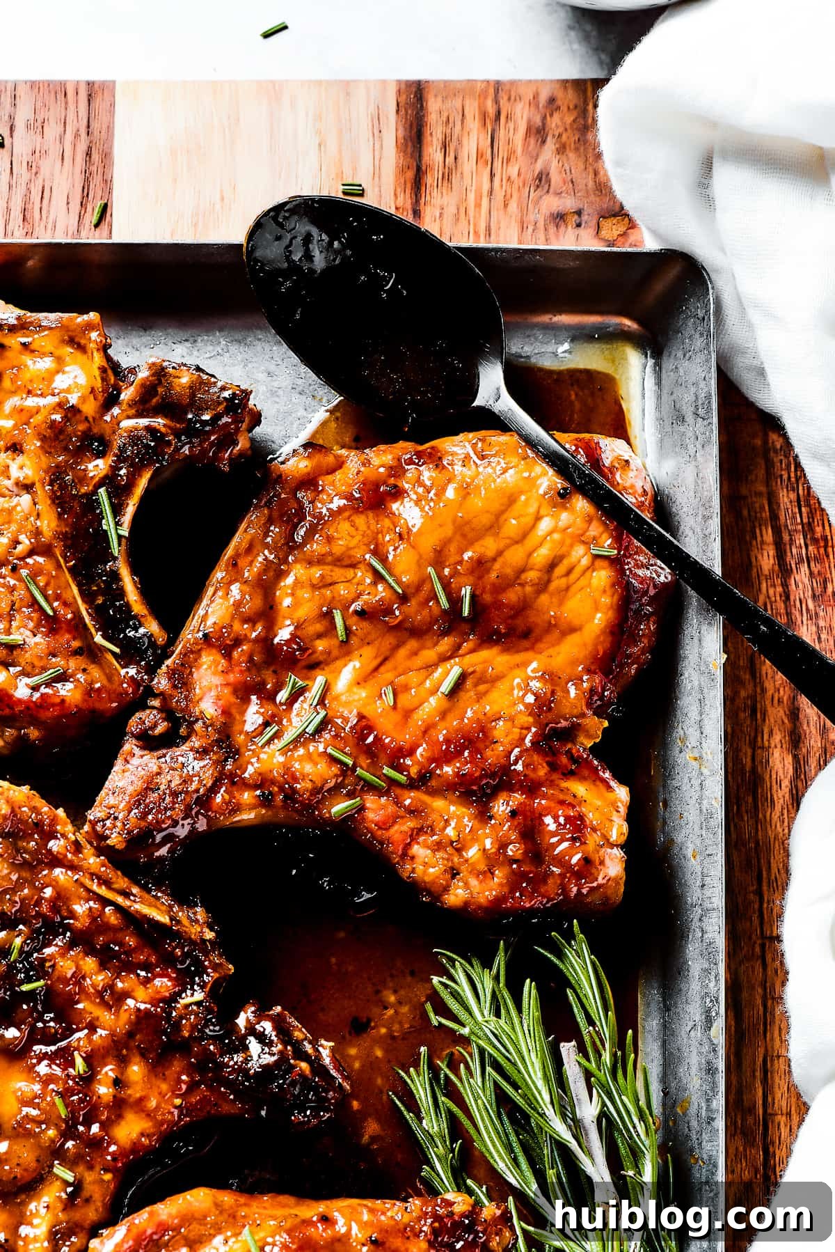 Gorgeous Brown Sugar Pork Chops may look fancy, but they are actually so simple to make! Savory, pan-fried chops with brown sugar glaze. A chef's hand spoons the thick brown sugar sauce generously over pan-fried pork chops on a serving platter.