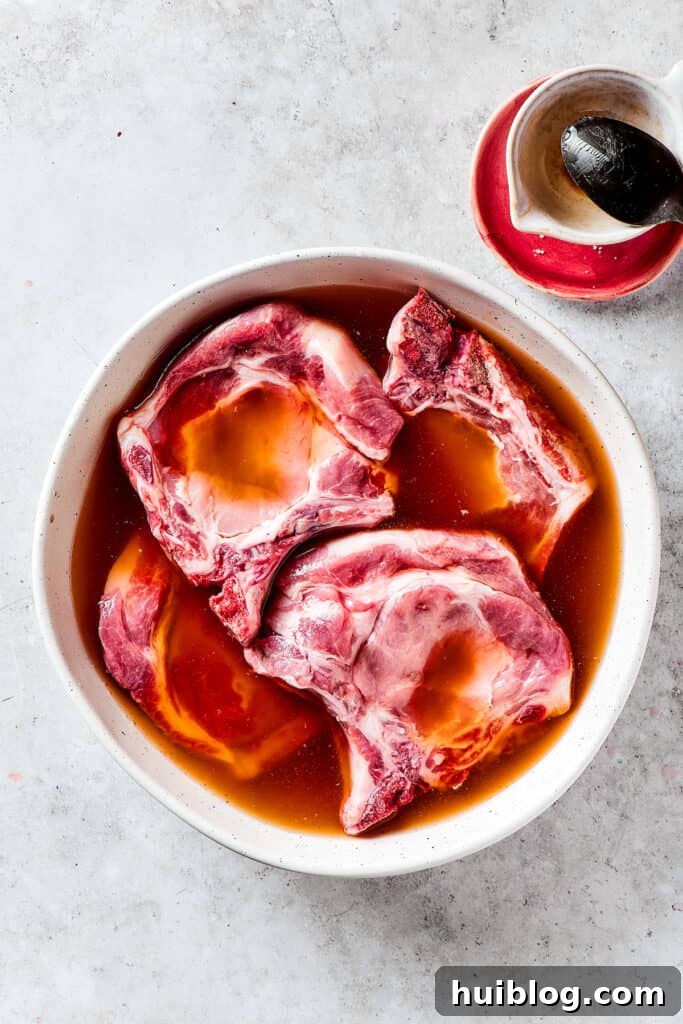 Gorgeous Brown Sugar Pork Chops may look fancy, but they are actually so simple to make! Savory, pan-fried chops with brown sugar glaze. Pork chops fully submerged in a brining solution within a clear bowl.