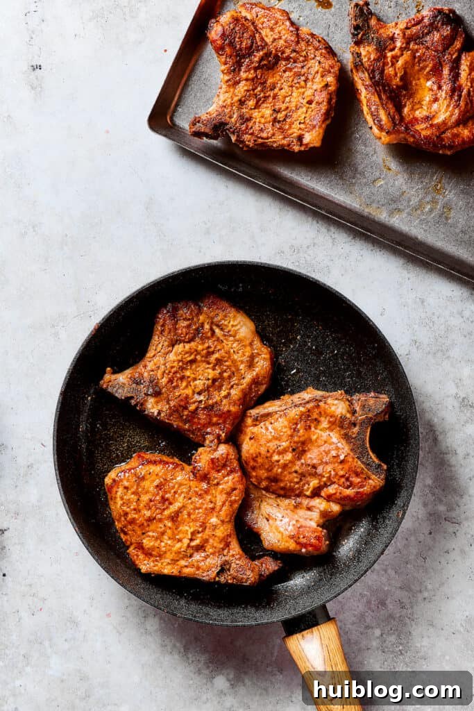 Gorgeous Brown Sugar Pork Chops may look fancy, but they are actually so simple to make! Savory, pan-fried chops with brown sugar glaze. Browned pork chops resting on a plate, while another batch cooks in a skillet.