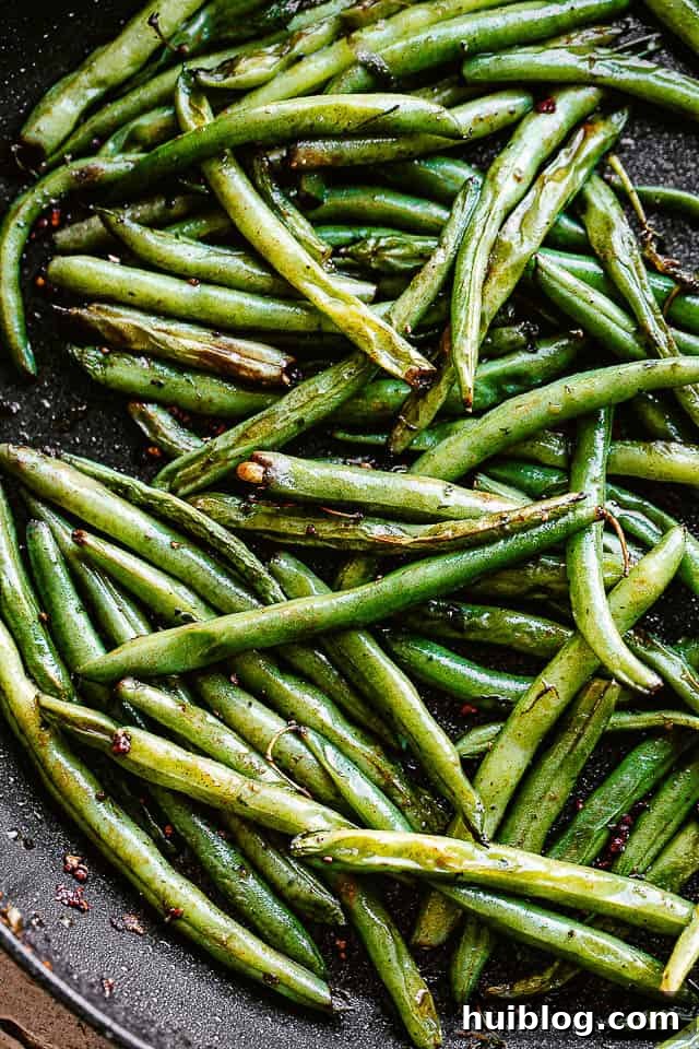 pan frying fresh green beans with oil and butter in a black skillet