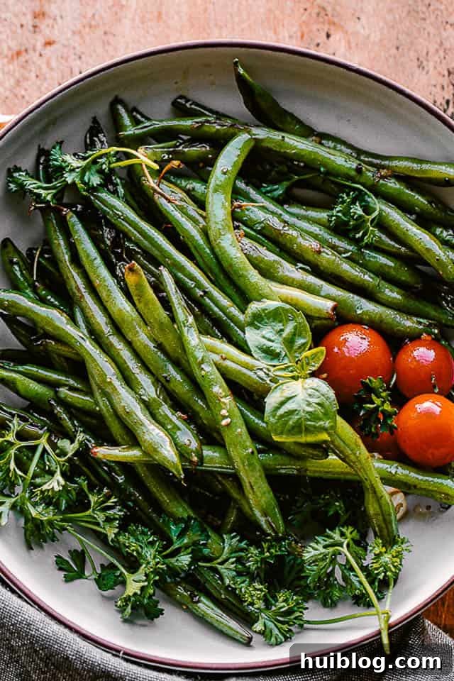 cooked green beans served in a bowl with fresh basil and cherry tomatoes as garnish