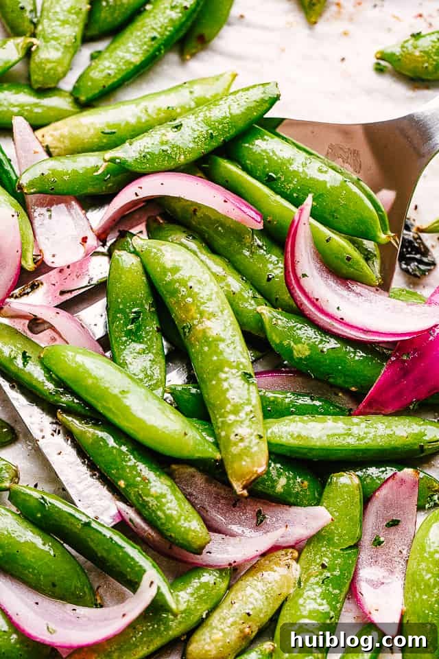 scooping up roasted snap peas from a baking sheet