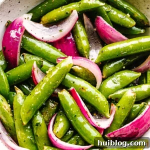 roasted sugar snap peas with red onions served in a cream bowl