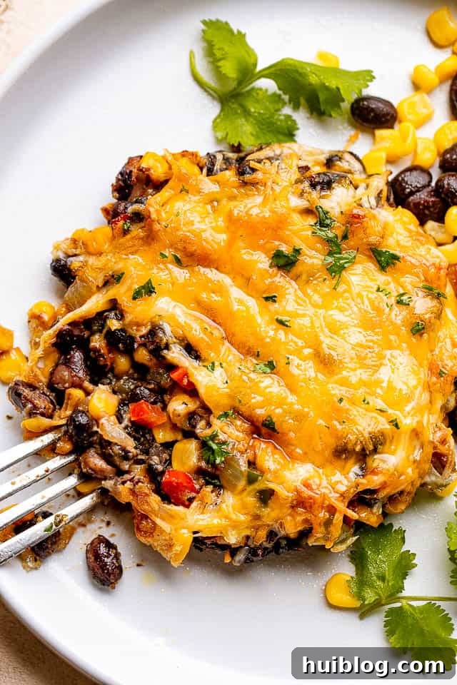 Fork next to a portobello mushroom stuffed with a vibrant mix of corn, black beans, and melted cheese, garnished with fresh herbs.