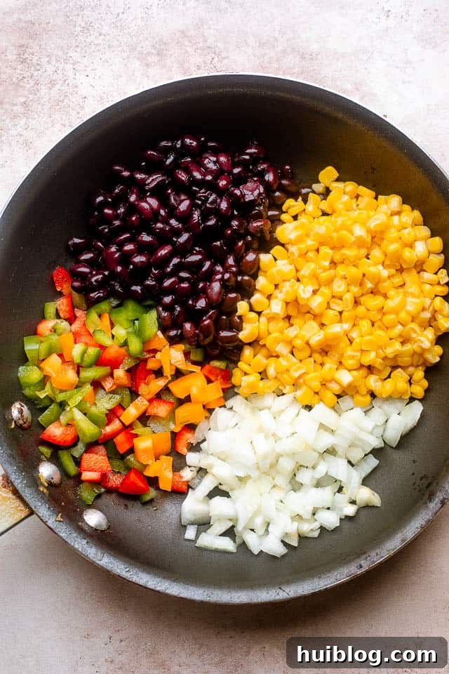 A frying pan filled with a colorful mixture of sautéing bell peppers, onions, black beans, and corn, creating a delicious filling.