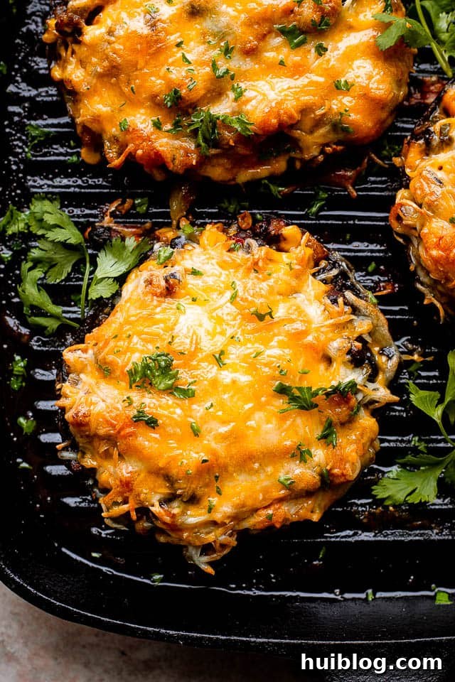 A close-up shot of grilled portobello mushrooms stuffed with black beans and corn, topped with perfectly melted and bubbly cheese.
