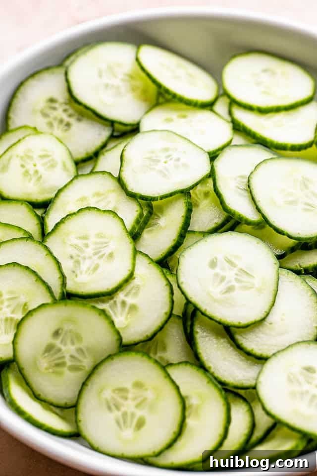 Crisp, thinly sliced cucumbers arranged neatly in a white bowl, prepped and ready to be transformed into a refreshing salad.