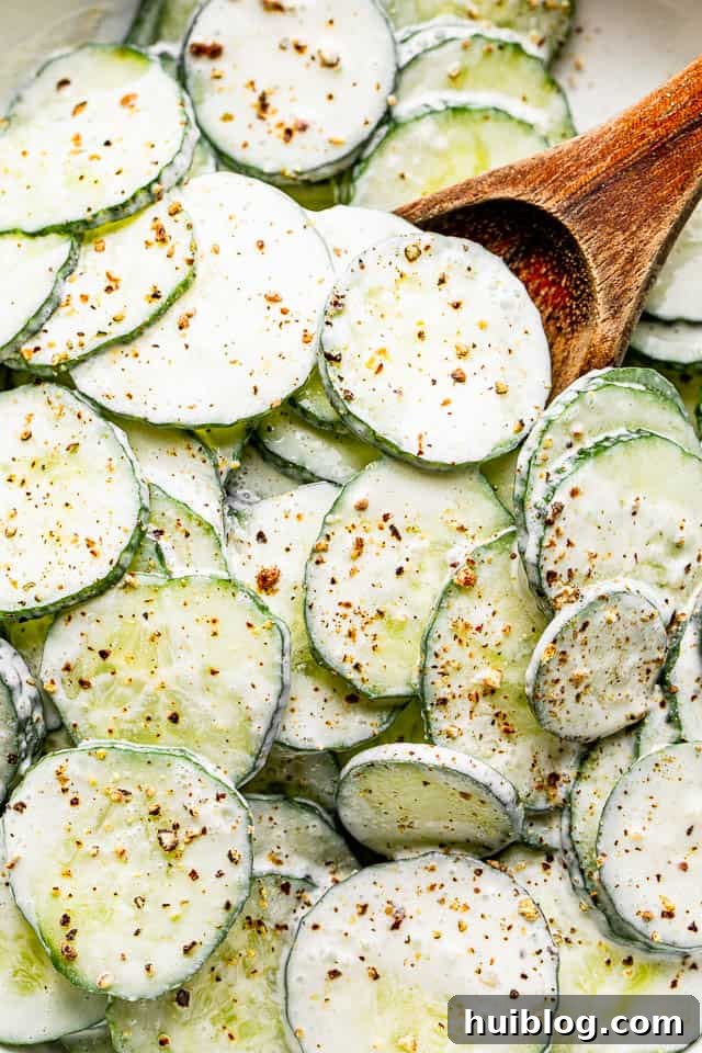 A close-up, top-down view of a wooden spoon scooping out a generous portion of creamy cucumber salad from a white bowl.