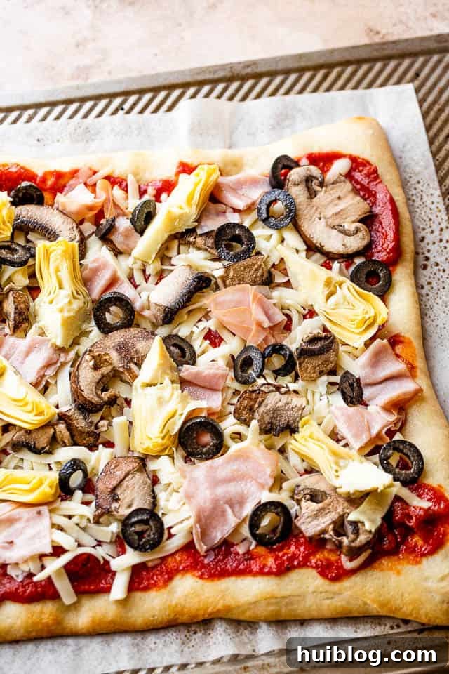 Smoky Capricciosa Pizza 5 tomato sauce, cheese, artichoke hearts, olives, and ham on top of pizza crust prepared for grilling