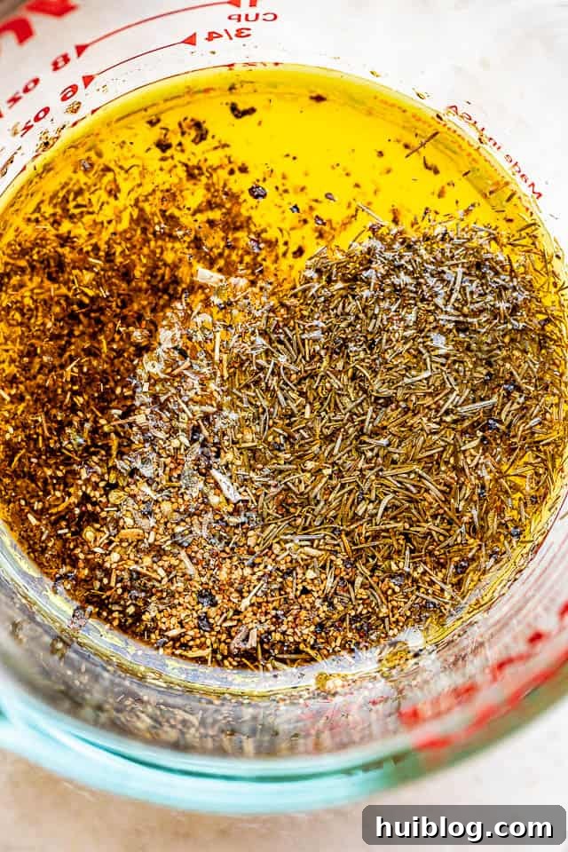 A glass measuring cup filled with a golden lemon garlic marinade, flecked with dried herbs, ready to be poured