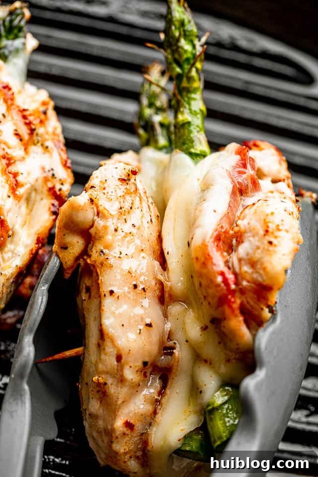 Close-up of a chicken breast stuffed with prosciutto, cheese, and asparagus, held together with tongs, showcasing the delicious filling.