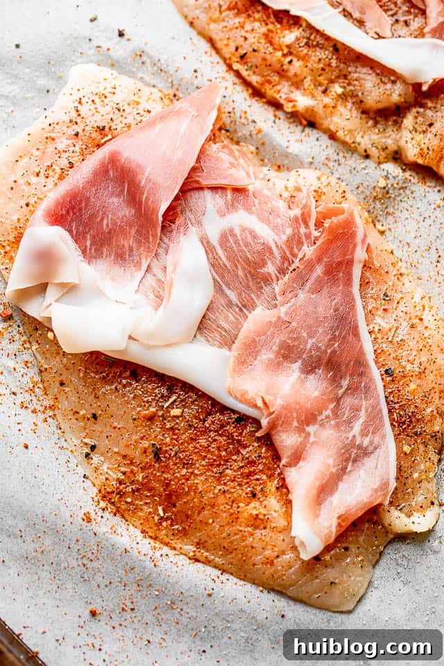 Slice of prosciutto laid over a raw, flattened chicken breast, ready for filling.