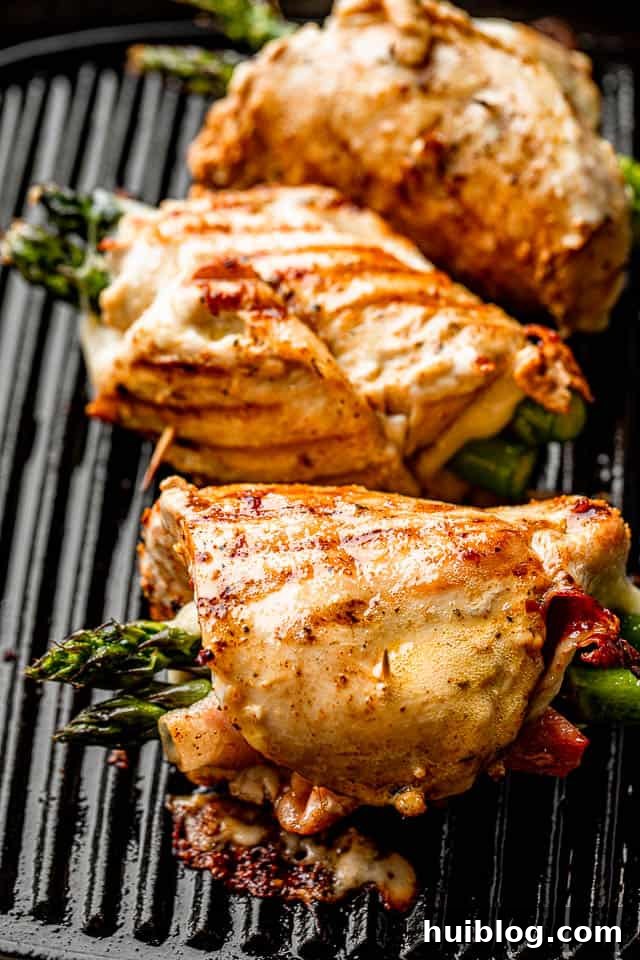 Three chicken roll-ups, stuffed with asparagus, prosciutto, and cheese, cooking on a grill pan, showing a delicious meal in progress.
