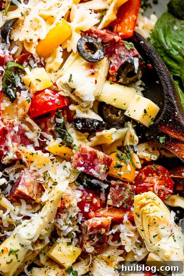 Italian Deli Pasta Salad 4 A close-up shot of a salad bowl brimming with colorful pasta, cheese cubes, salami cubes, halved cherry tomatoes, and black olives.