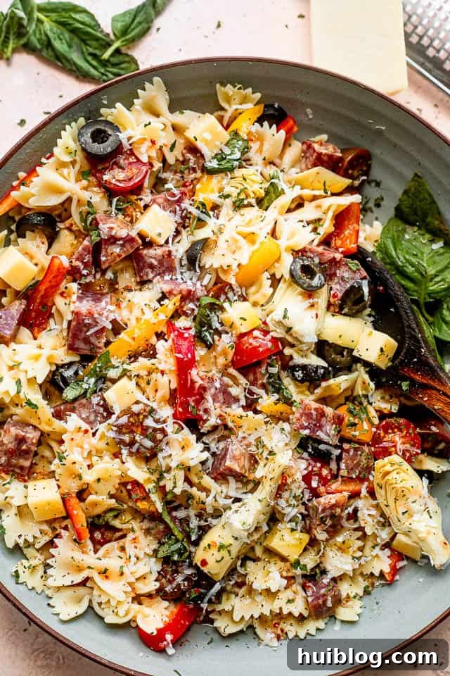 Italian Deli Pasta Salad 5 Overhead view of a wooden spoon resting in a bowl full of Italian Antipasto Pasta Salad, featuring pasta, cheese cubes, salami, tomatoes, and olives.