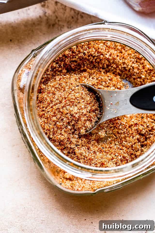 A silver tablespoon rests in a glass jar filled with a delicious pork seasoning rub, showcasing the key ingredients.