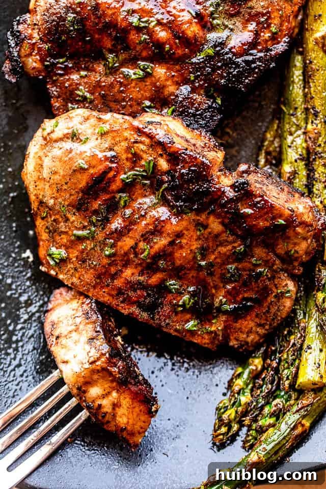 Plated juicy grilled pork chops served on a black plate alongside fresh green asparagus, ready to eat.