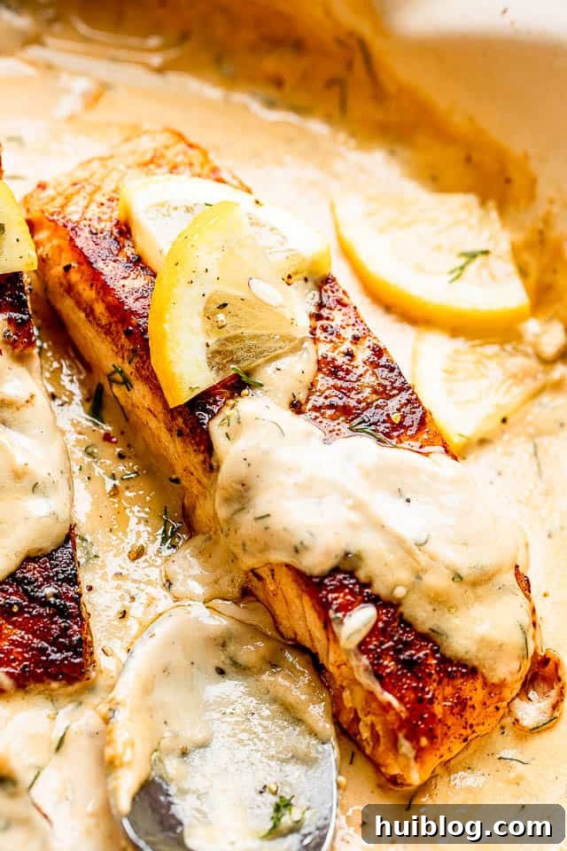close up of cooked salmon fillet topped with creamy dill sauce and a slice of lemon