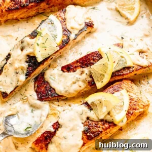 white pan with four salmon fillets topped with lemon slices and cream sauce
