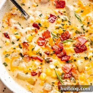 silver spoon inside corn chowder soup in a bowl topped with bacon, green onions, and parsley