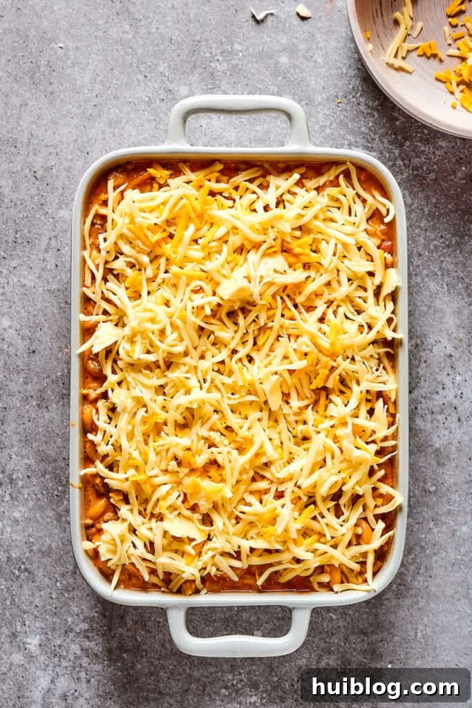 An overhead shot of a casserole dish generously covered in shredded cheese, ready for baking.