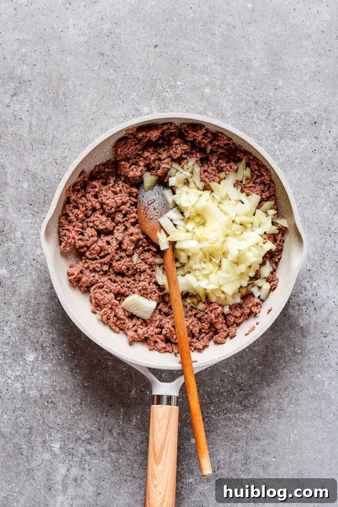Adding diced onion to a skillet of sizzling ground beef.