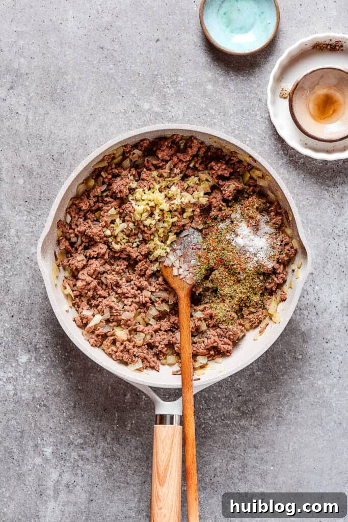 Sprinkling seasonings into a skillet with browned beef and onions, infusing rich flavors.