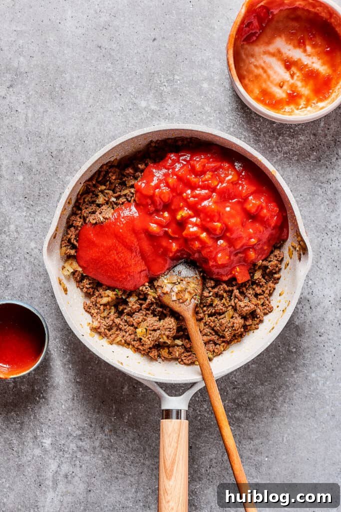 Adding rich tomato puree and flavorful diced tomatoes to the seasoned ground beef in a skillet.