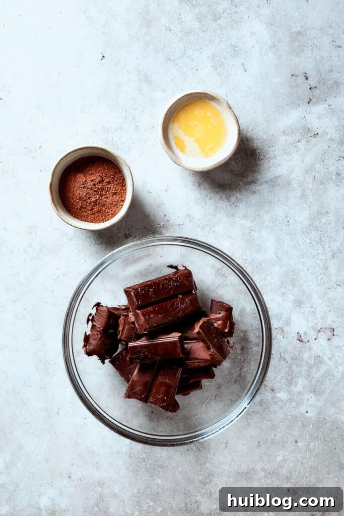 Chocolate in a glass bowl next to a dish of melted butter and a dish of cocoa powder.