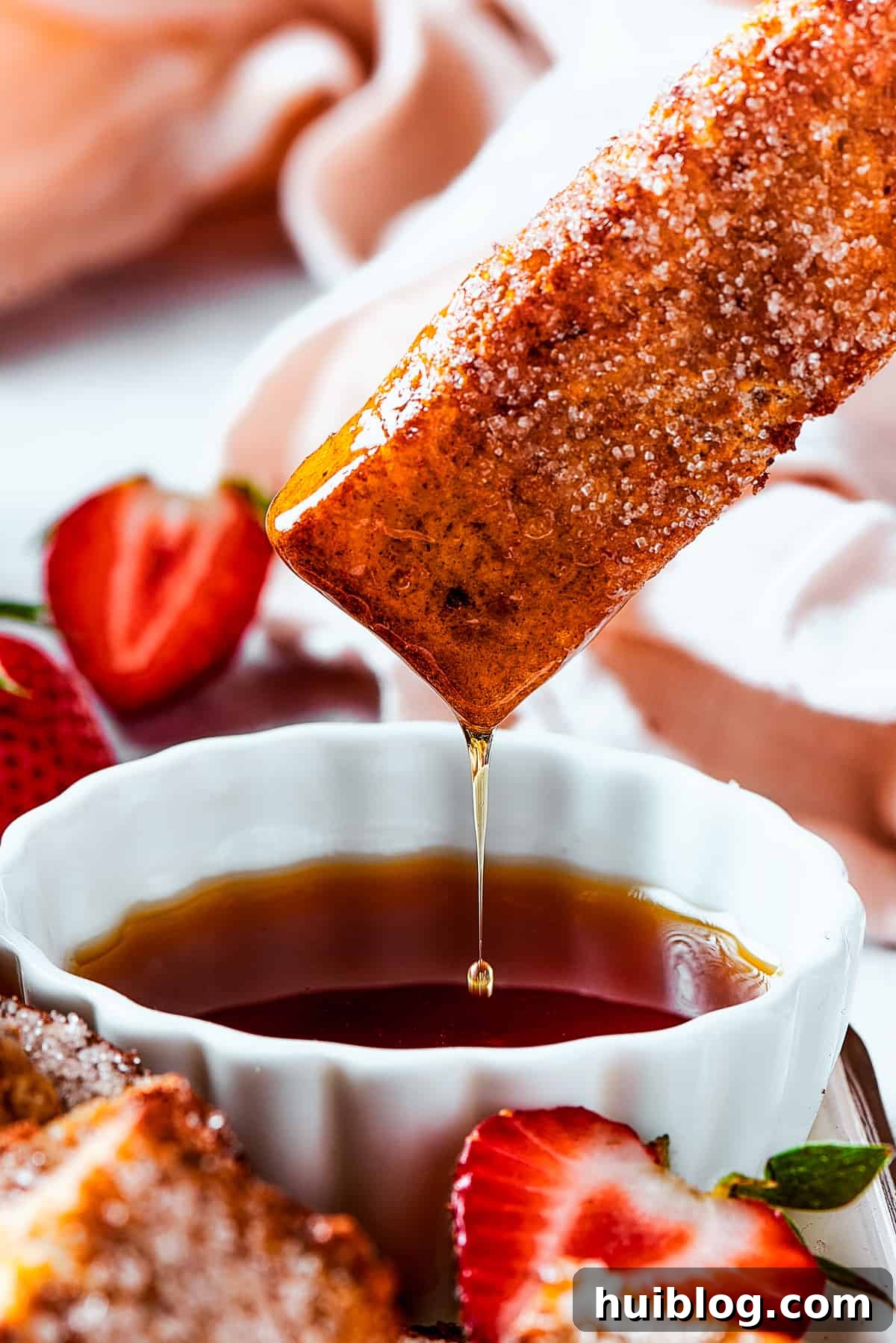 Lifting a piece of toast from a cup of syrup, with the syrup dripping back into the cup.