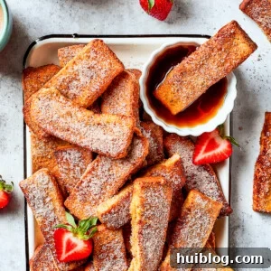 A tray of French toast sticks with maple syrup and strawberries. One stick is dunked in the syrup.