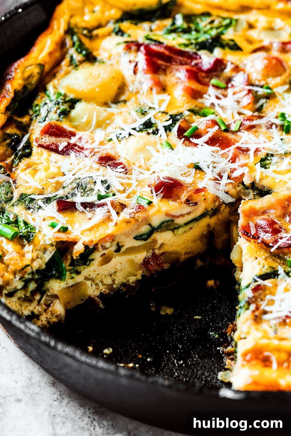 A baked frittata in a cast-iron skillet with a slice elegantly removed, revealing its delicious layers.