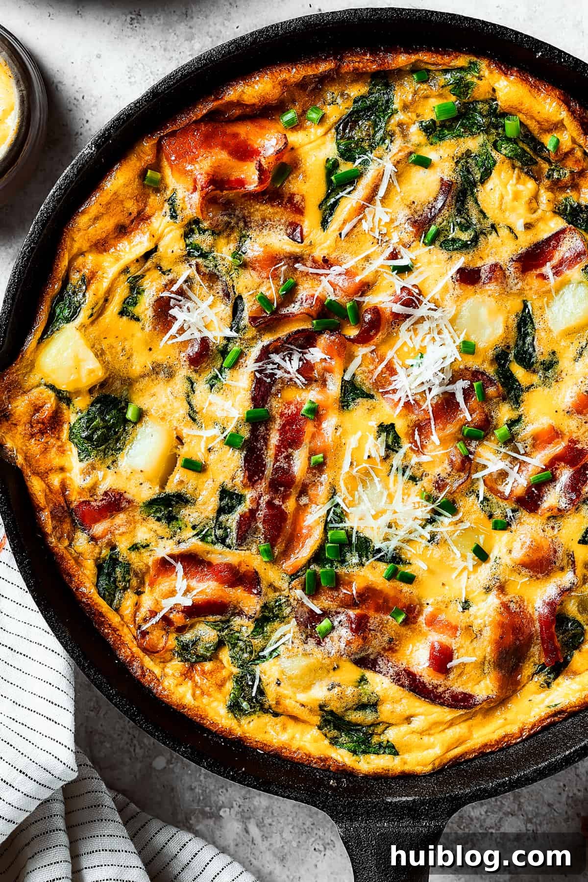 Close-up overhead shot of a freshly cooked frittata in a cast-iron pan, showcasing its golden-brown top and vibrant fillings.