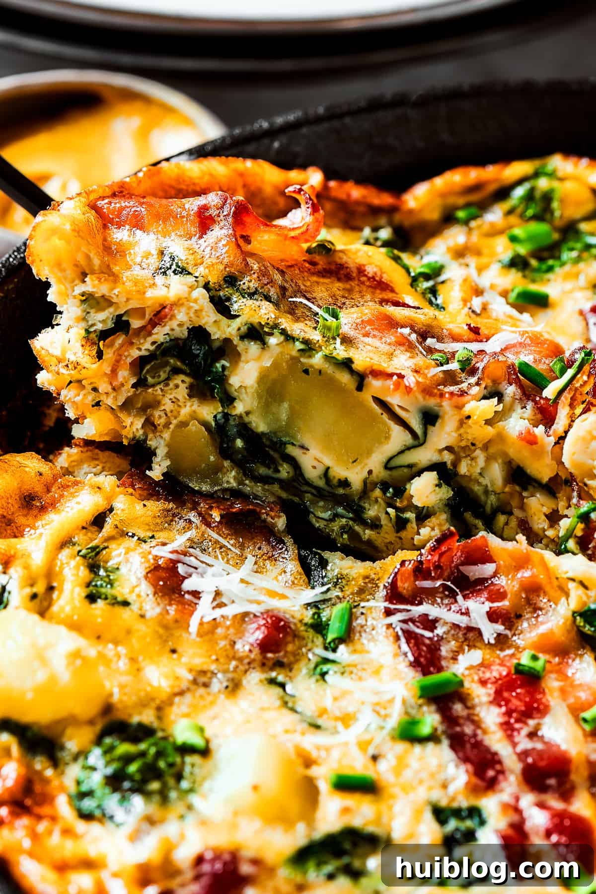 A hand lifting a perfect slice of Spinach, Bacon, and Potato Frittata out of a cast-iron pan.