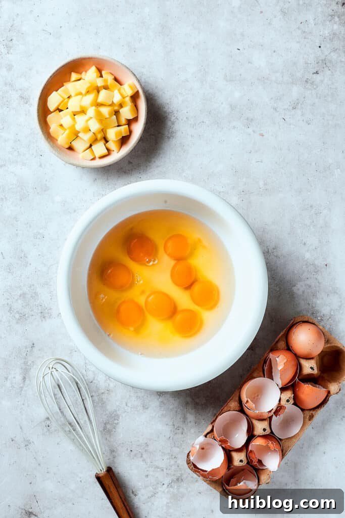 Eggs cracked into a bowl, with cooked potatoes nearby on the table, preparing for the frittata.