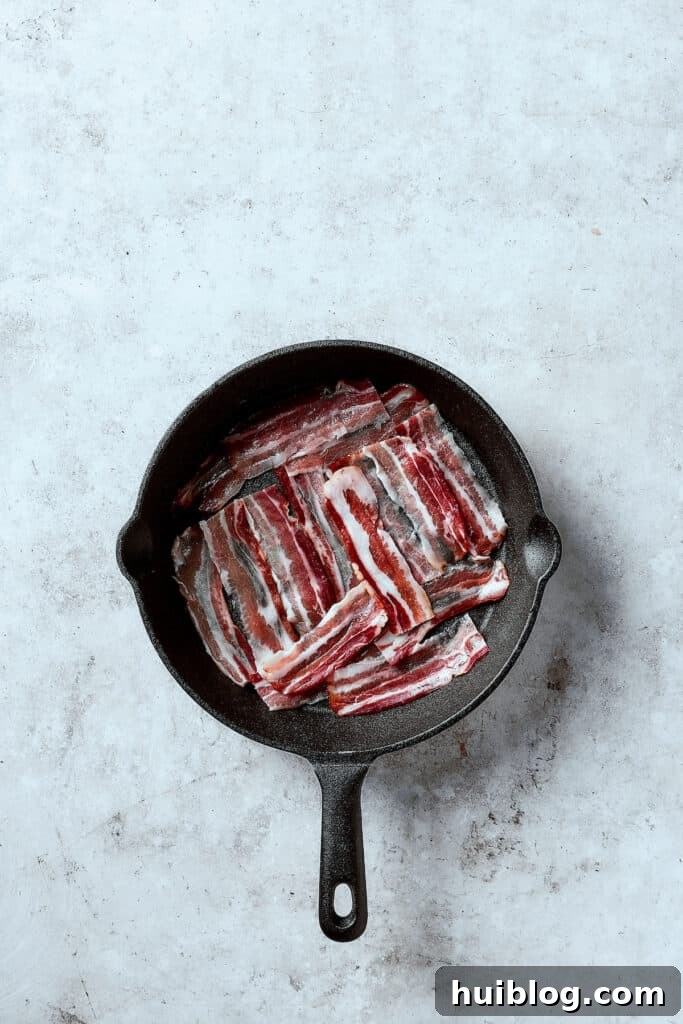 Bacon slices frying in a hot skillet, becoming crispy.