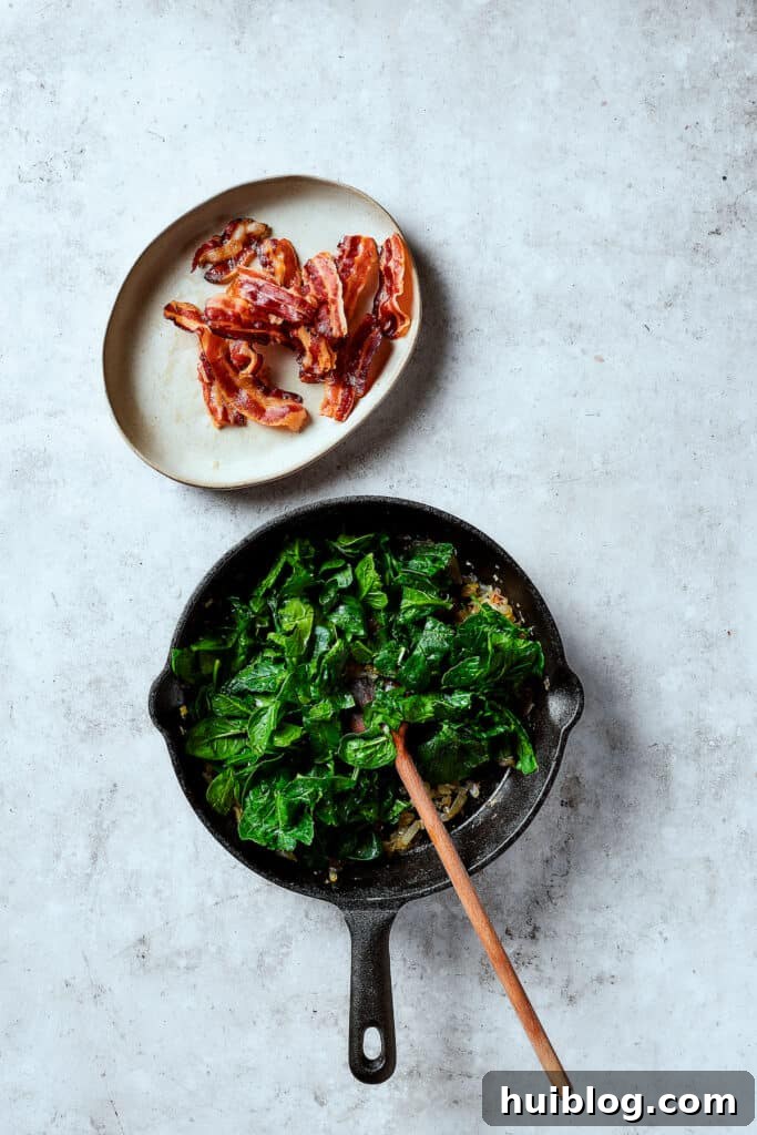 Fresh spinach wilting in a skillet with sautéed onion and garlic.