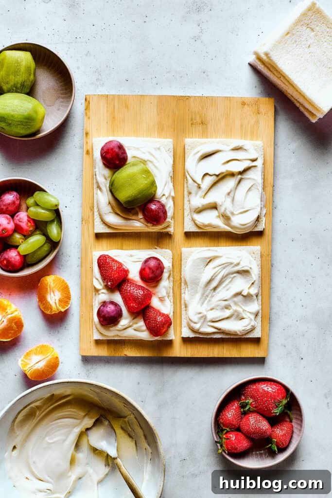 Arranging colorful fruit slices on a layer of whipped cream on white bread.