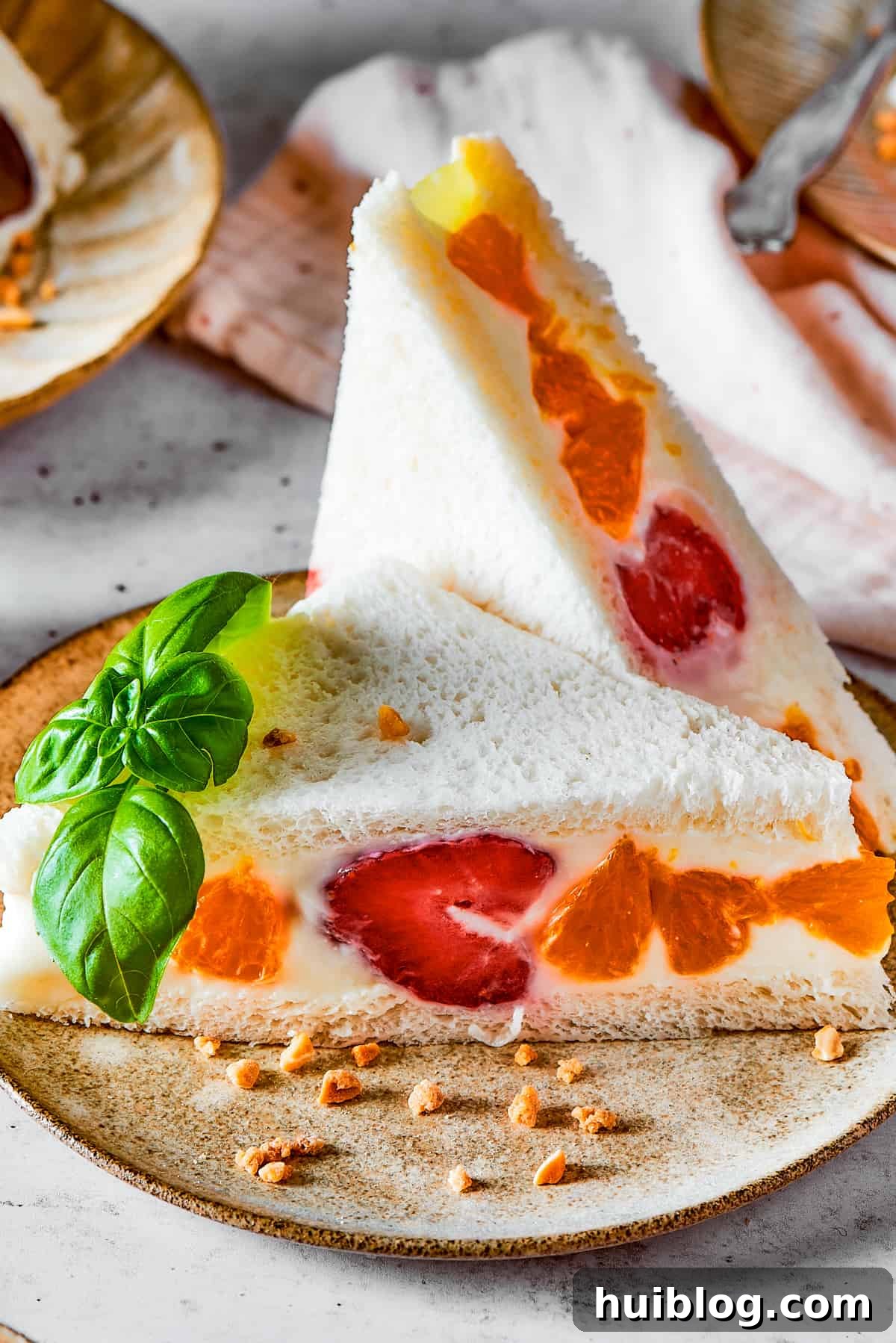 A vibrant fruit sando featuring white bread, bright mandarin oranges, and strawberries, showing a perfect cross-section.