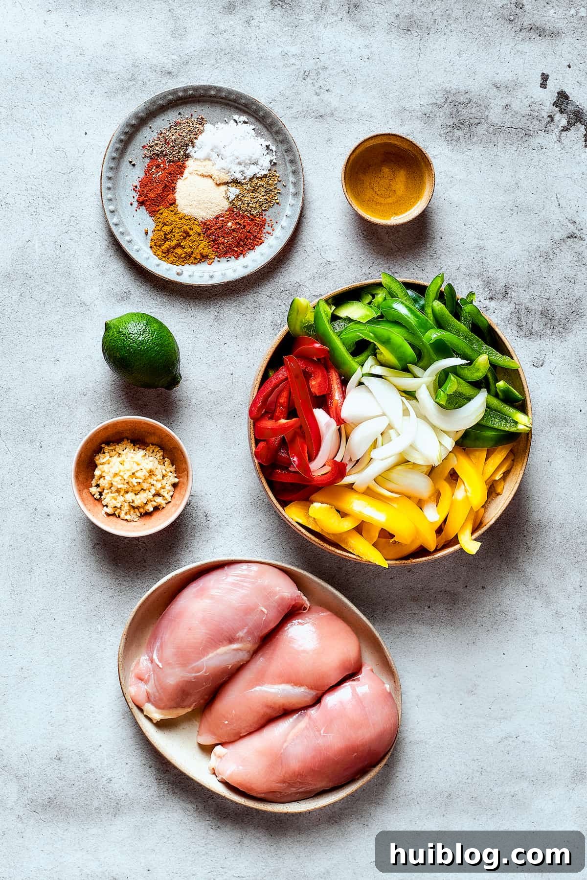 All the fresh ingredients for crockpot chicken fajitas, including chicken, colorful bell peppers, onion, lime, and various spices, arranged on a rustic wooden surface.