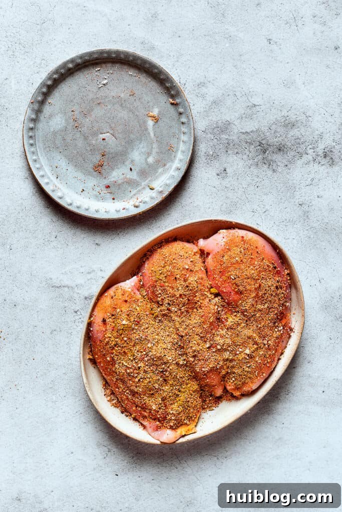 Raw chicken breasts generously coated with a savory fajita seasoning blend, ready for the slow cooker.